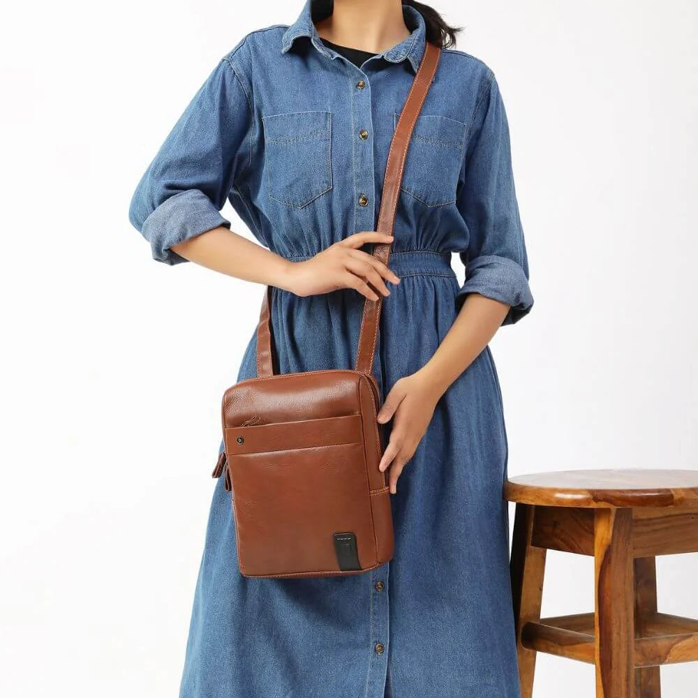 Woman wearing beige trench coat and carrying a brown leather Tuscan messenger bag with crossbody strap.