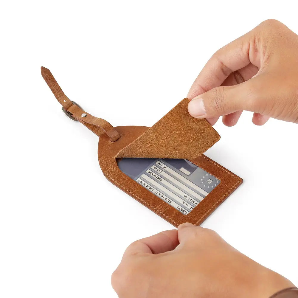 Top view of tan leather luggage tag showing clear ID window and sturdy metal buckle strap.