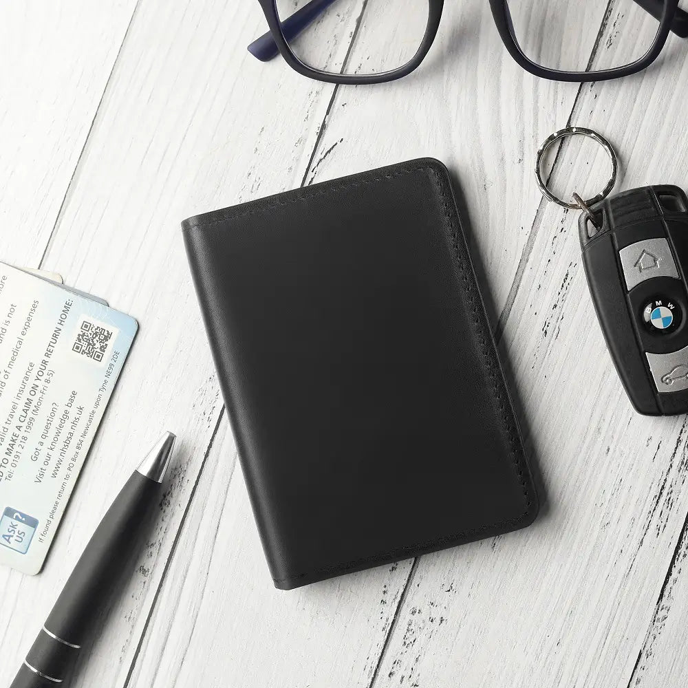 Black leather vertical card wallet on desk beside glasses, pen and card