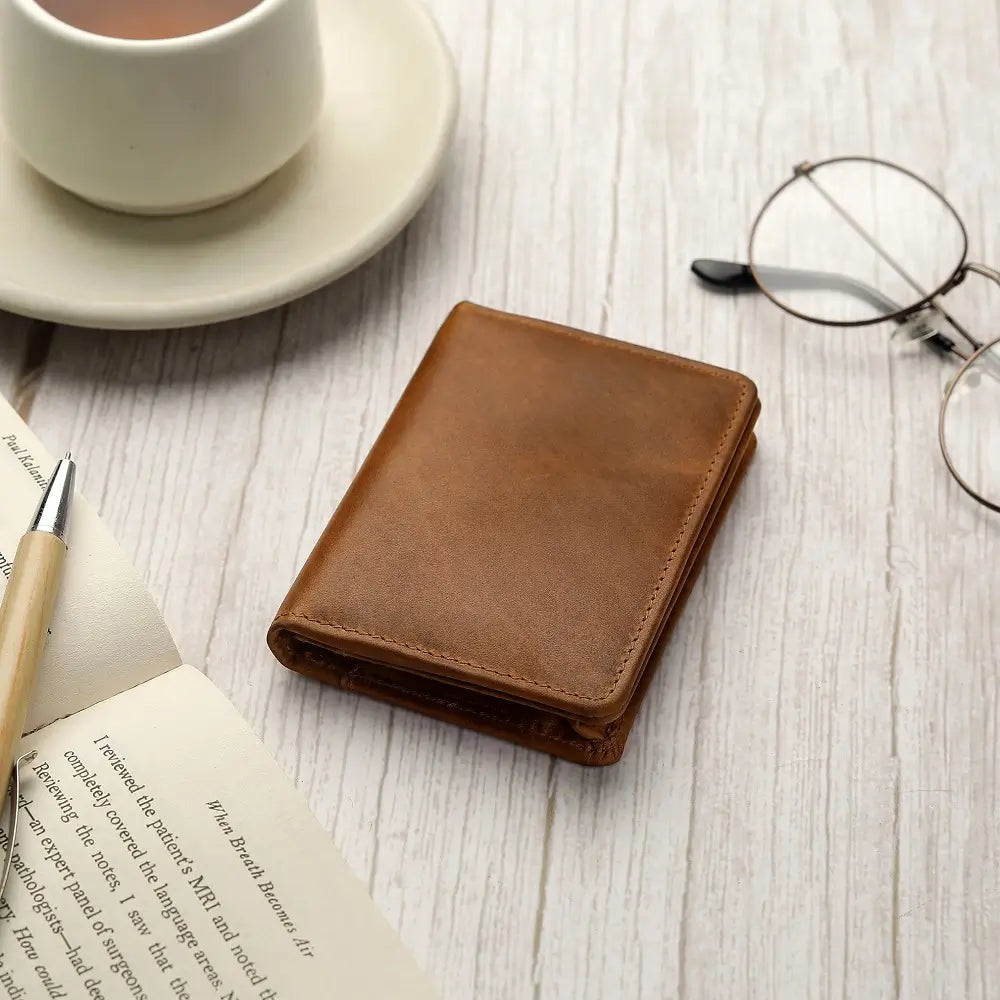 Tan leather Mayfair 2511 credit cardholder placed on a wooden café table beside a coffee cup and glasses.