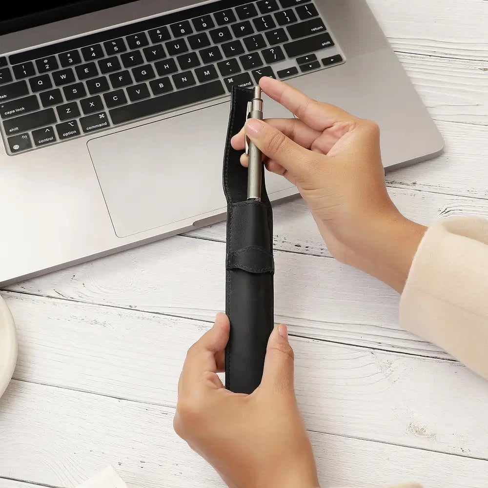 Black leather pen holder placed on an open diary beside a pen and laptop, styled for a modern office desk.