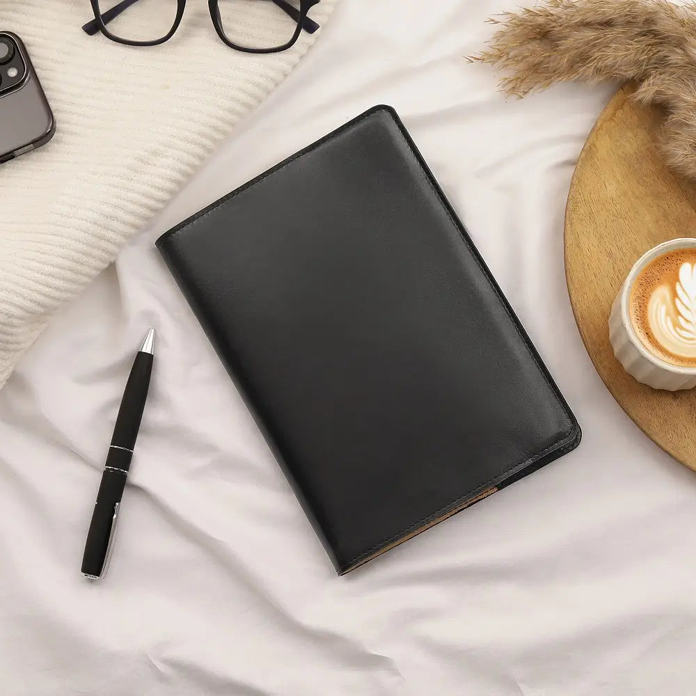 Black Leather Diary Cover Mayfair 2519 placed on a work desk beside a pen and coffee cup in a lifestyle setting.