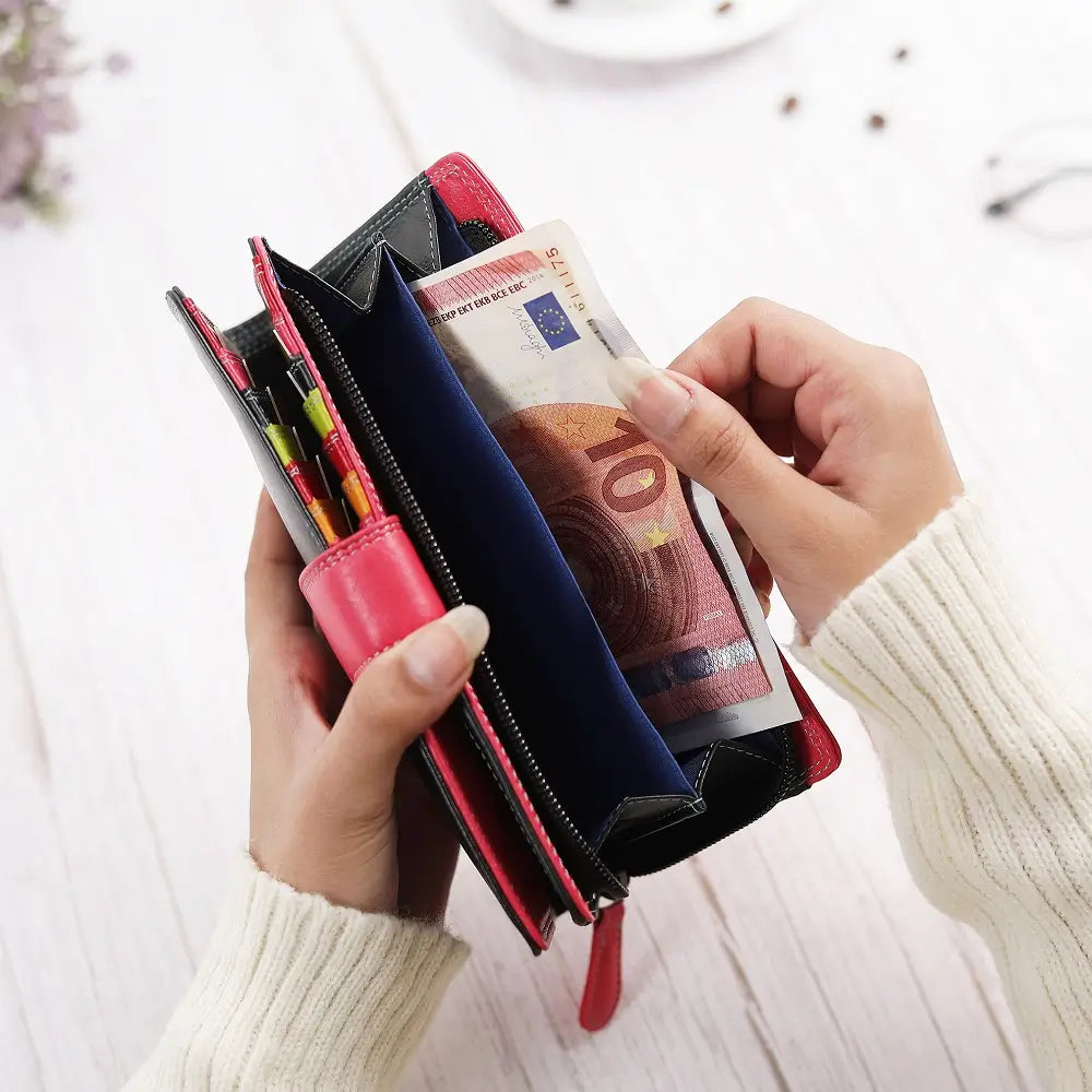 Person holding a black wallet with money and pens on a light background