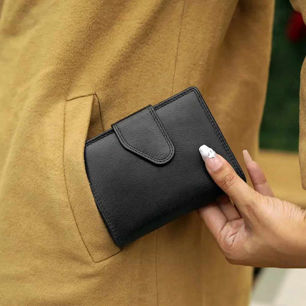 Person holding a black wallet against a beige background