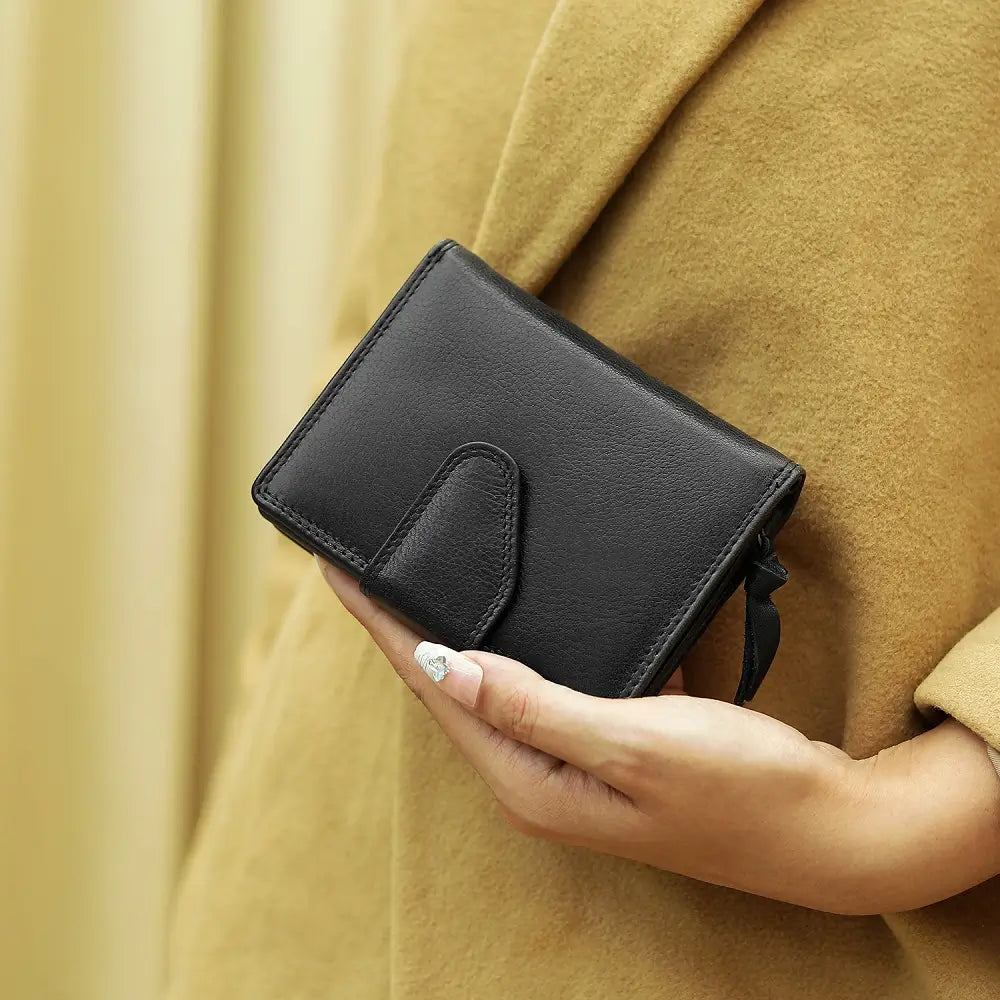 Person holding a black leather wallet against a beige background