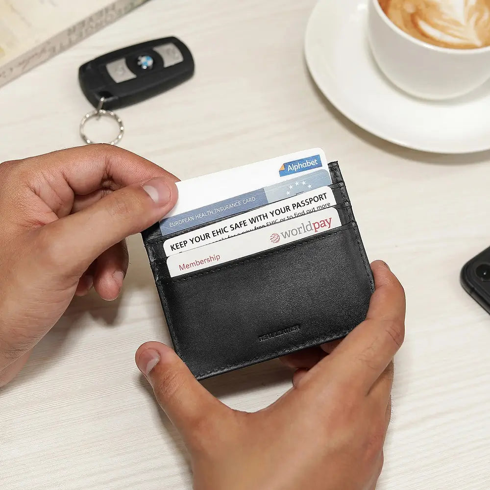 Person holding a black card holder with cards on a table with a cup of coffee and car keys.