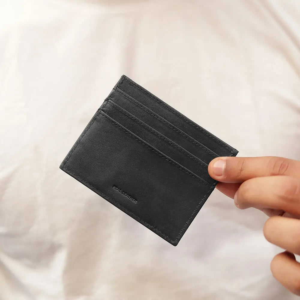 Black leather cardholder held by a hand against a light background
