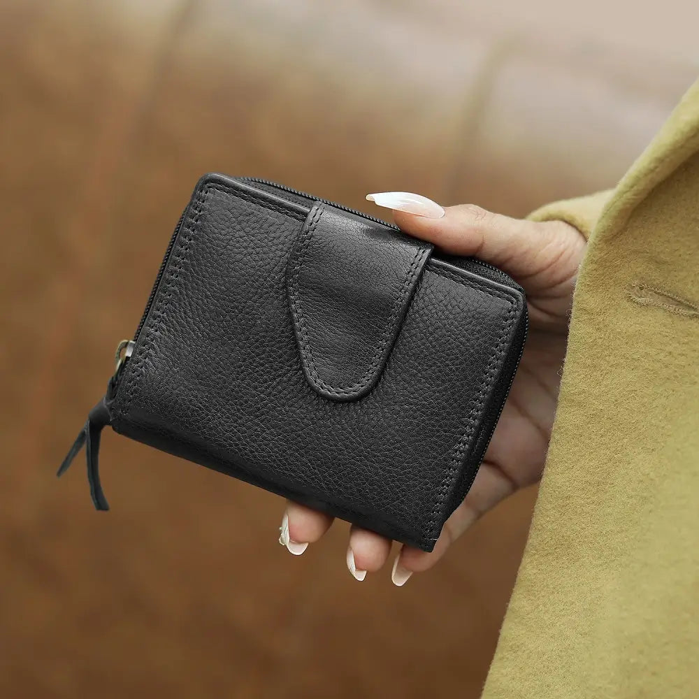 Person holding a black wallet with money and cards, with a cup of coffee and sunglasses in the background.