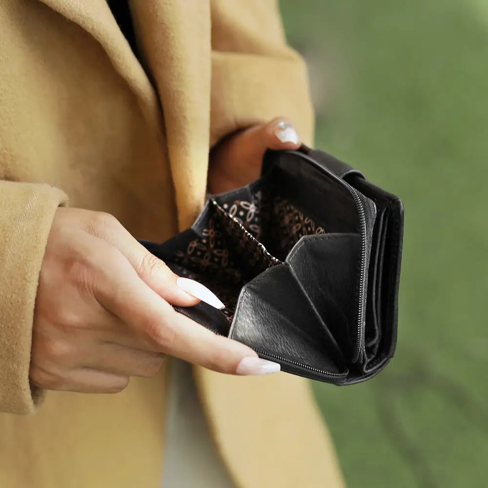 Person holding a black wallet with a blurred green background