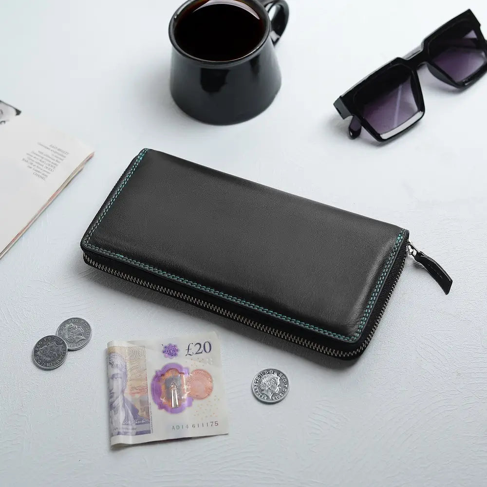 Black purse on a white surface with coins, banknotes, sunglasses, and a mug.