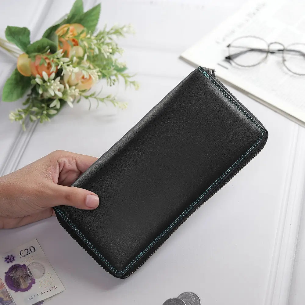 Black purse held by a hand on a white surface with flowers and glasses in the background