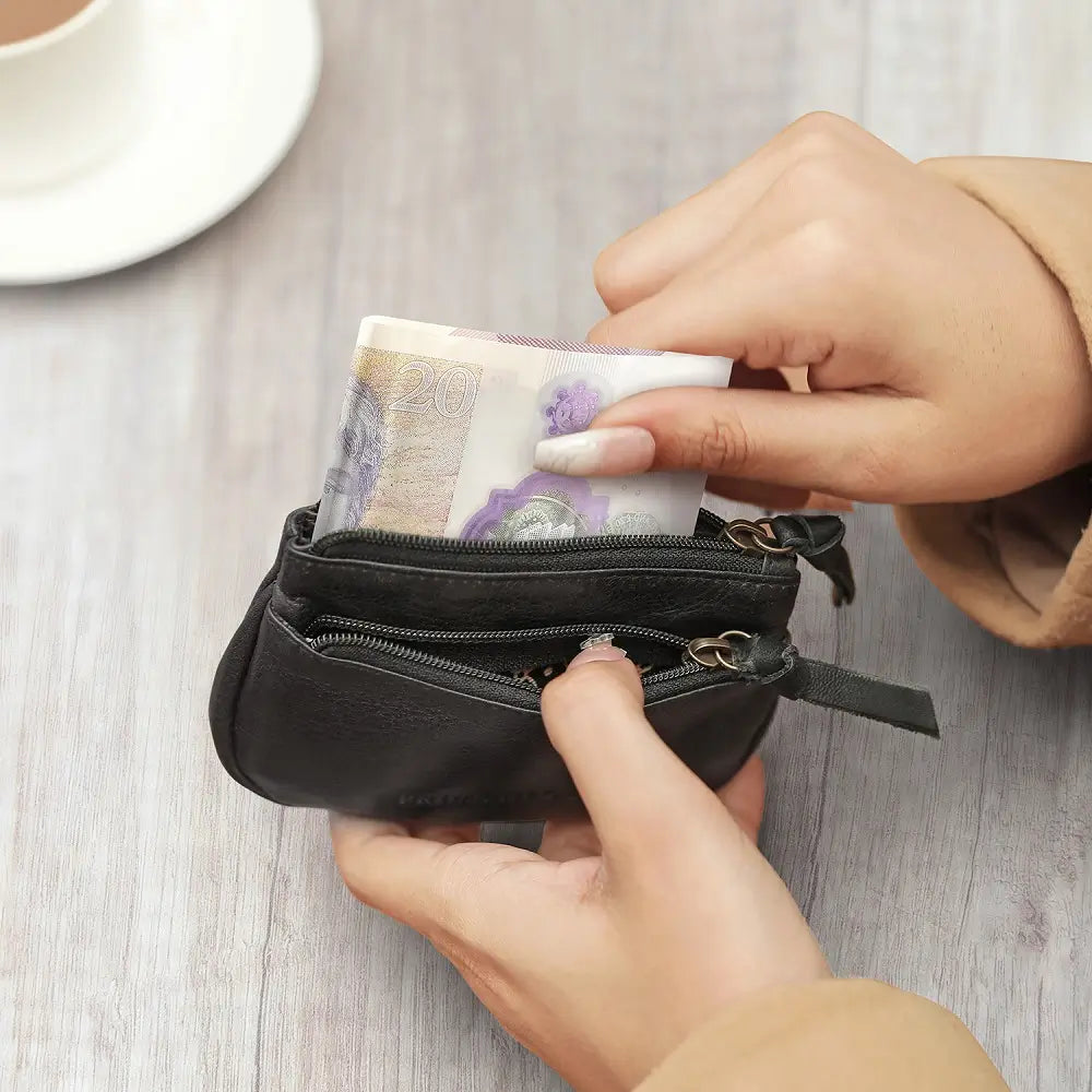 Person holding a black wallet with money on a light wooden surface