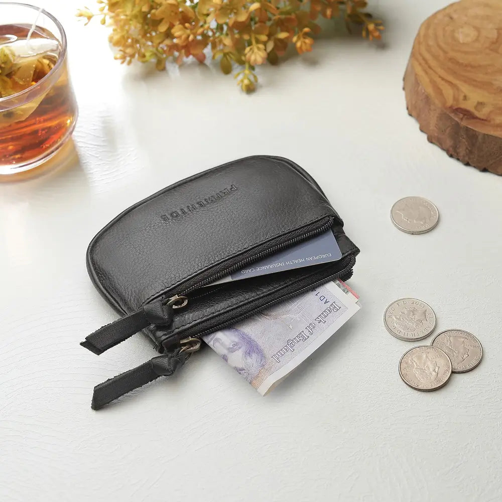 Black leather wallet with money and coins on a light surface with a glass of tea and flowers in the background.