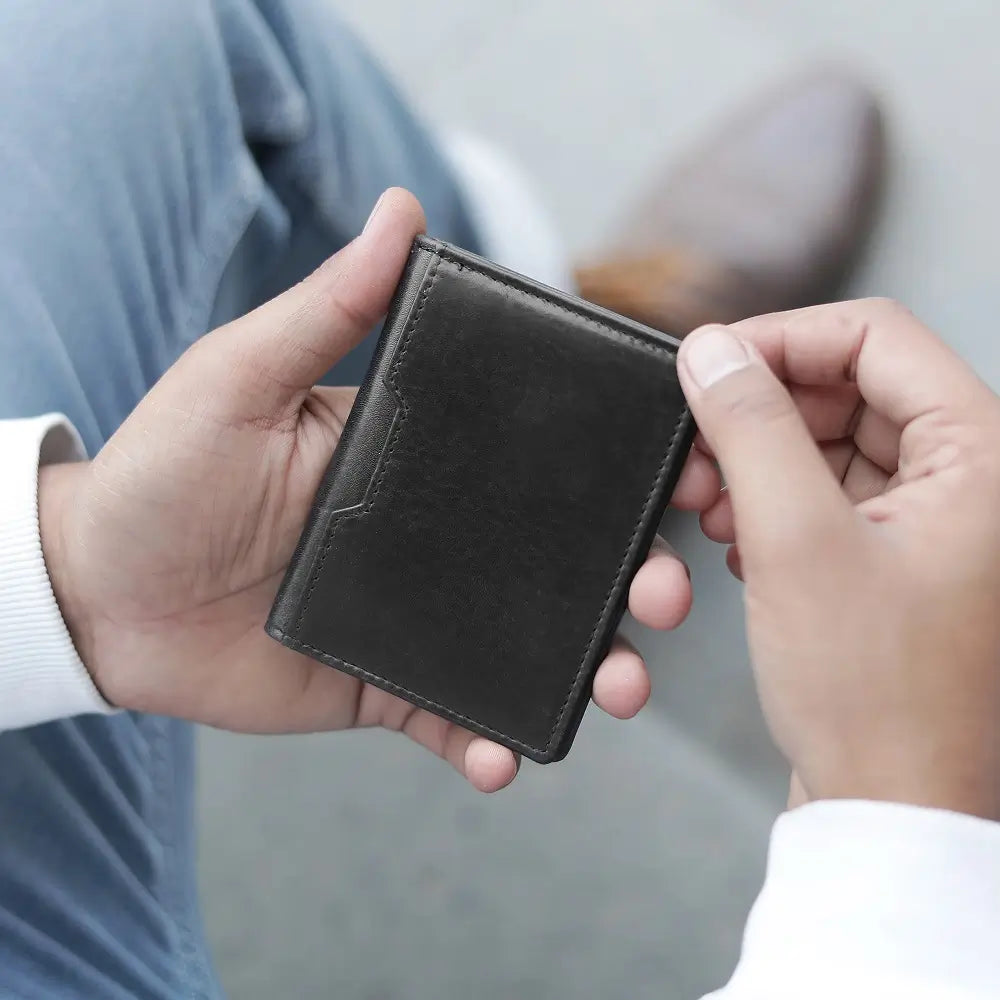 Two hands holding a black leather credit card holder against a neutral background