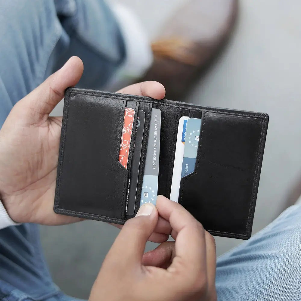 Person holding a black leather credit card holder with cards inside, blurred background