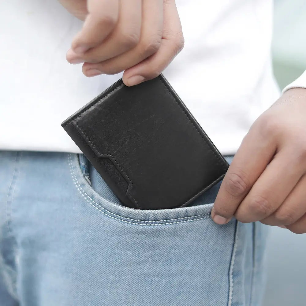 Person inserting a black credit card holder into a blue jeans pocket.