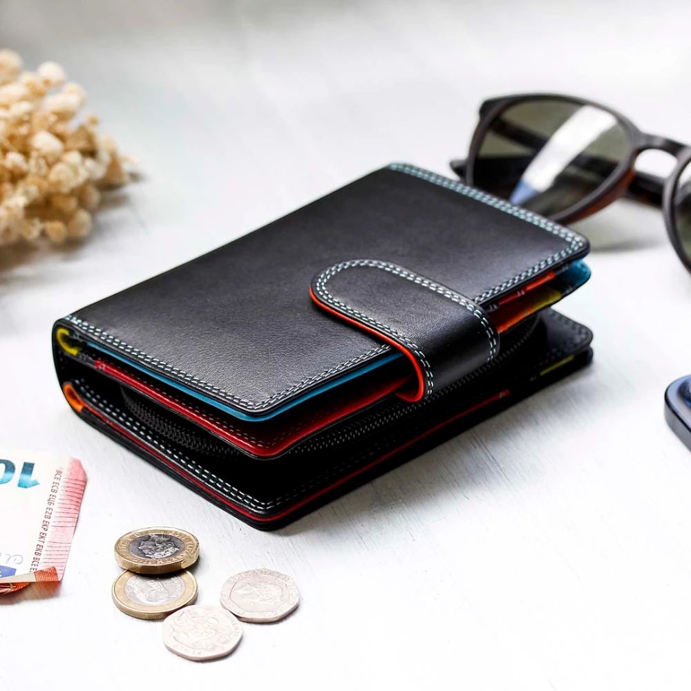 Black leather wallet with colorful stitching on a white surface with coins and sunglasses.