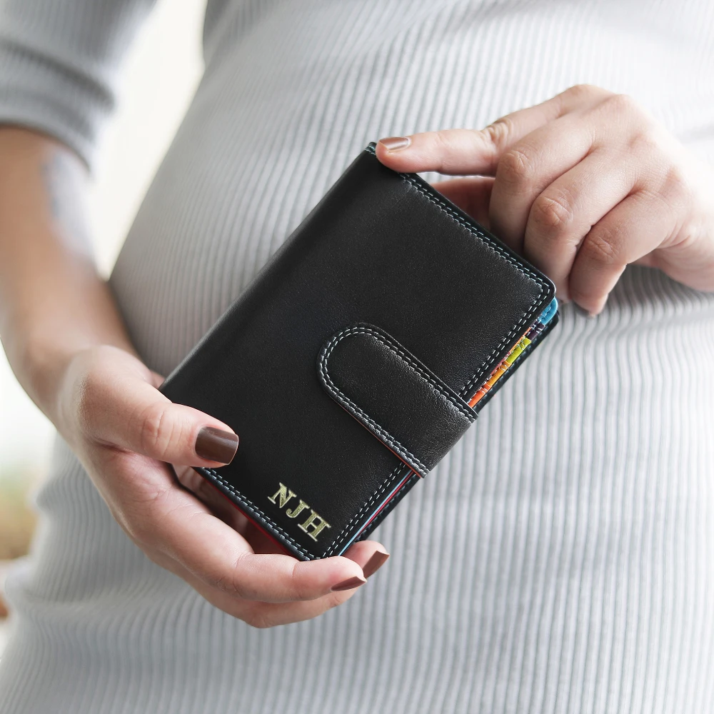 Person holding a black wallet with initials on a light gray background