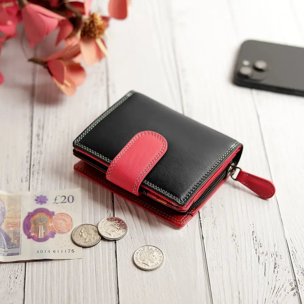 Black and red wallet with coins and a banknote on a wooden surface