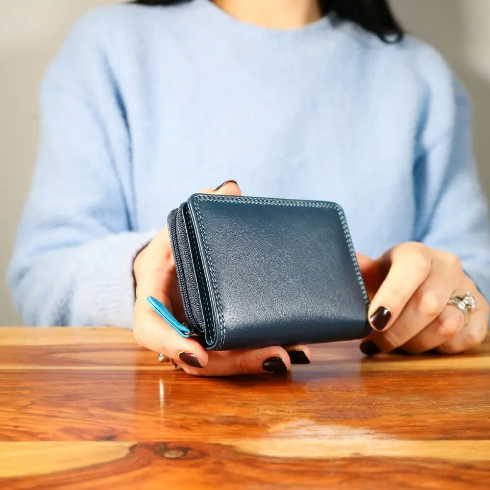 Person holding a blue wallet on a wooden table