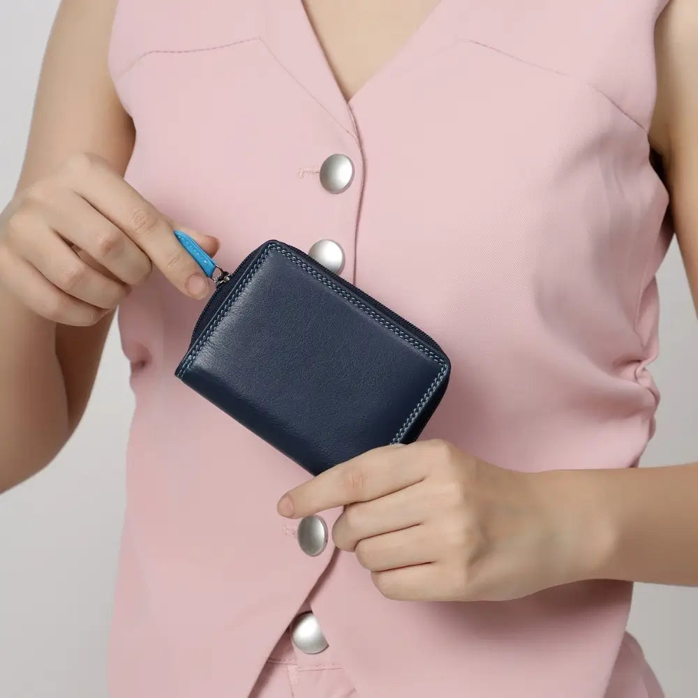 Person holding a navy blue wallet against a light pink background