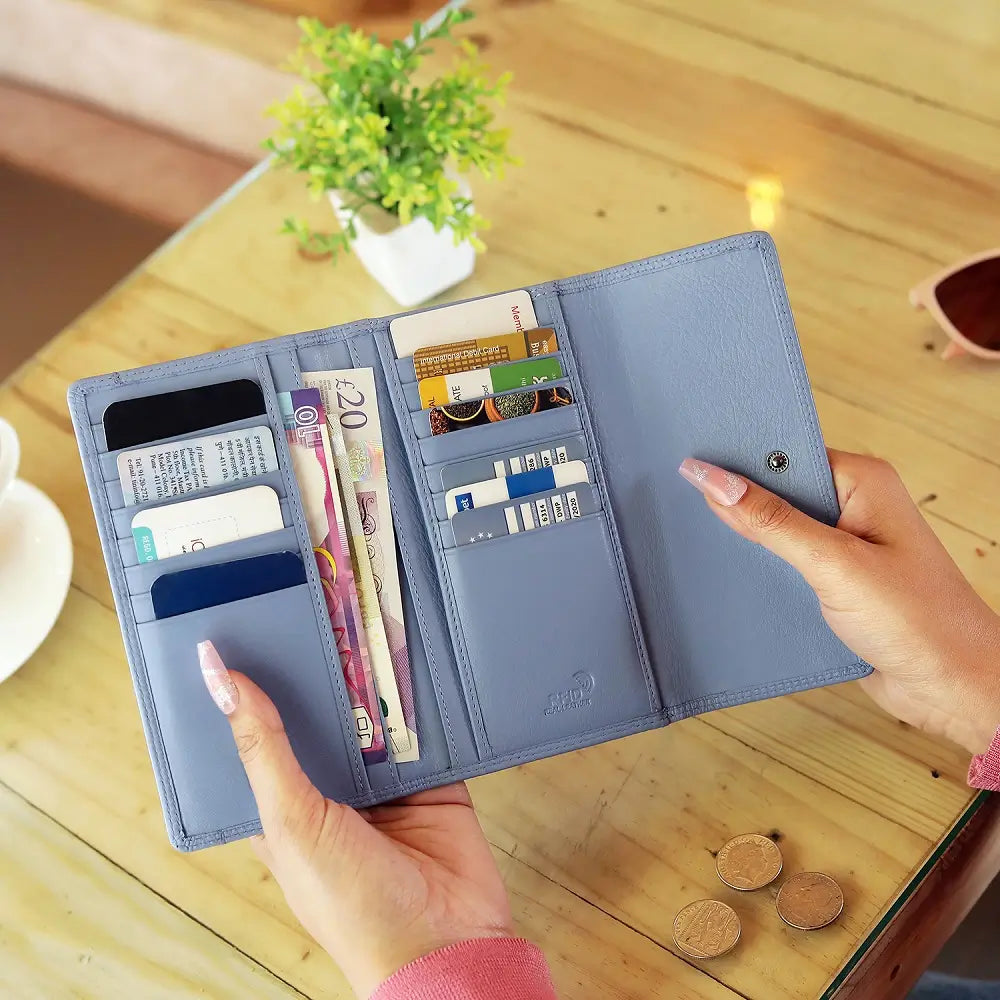 Blue wallet with various cards and money held by a hand on a wooden table.