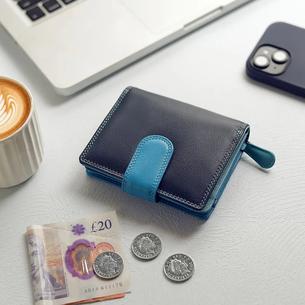Blue wallet with coins and banknotes on a white surface with a laptop and phone in the background.