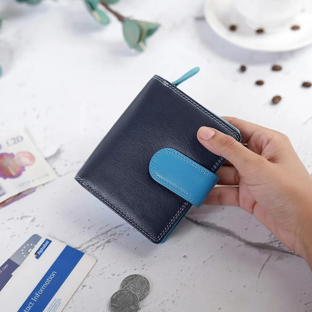 Hand holding a blue wallet with coins and cards on a light surface
