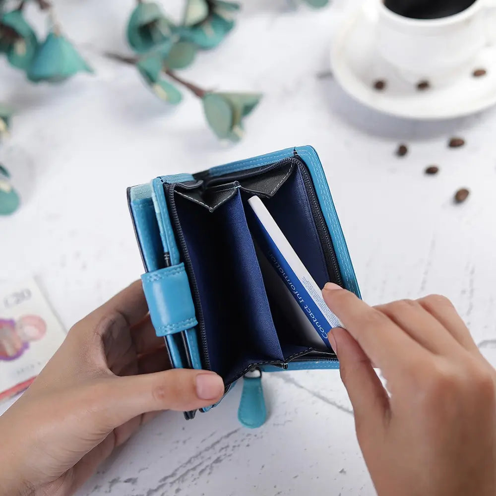 Blue wallet held by hands with a coffee cup and flowers in the background