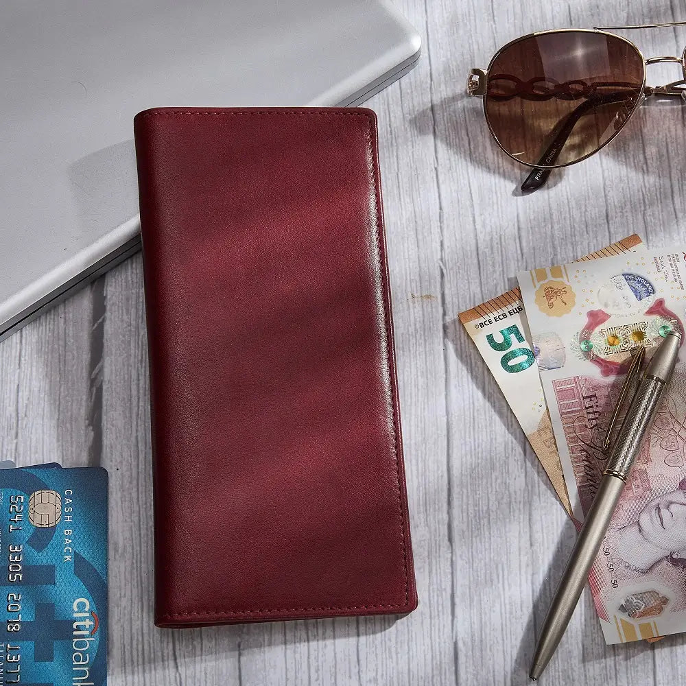 Bordeaux wallet on a wooden surface with money, sunglasses, and a pen.