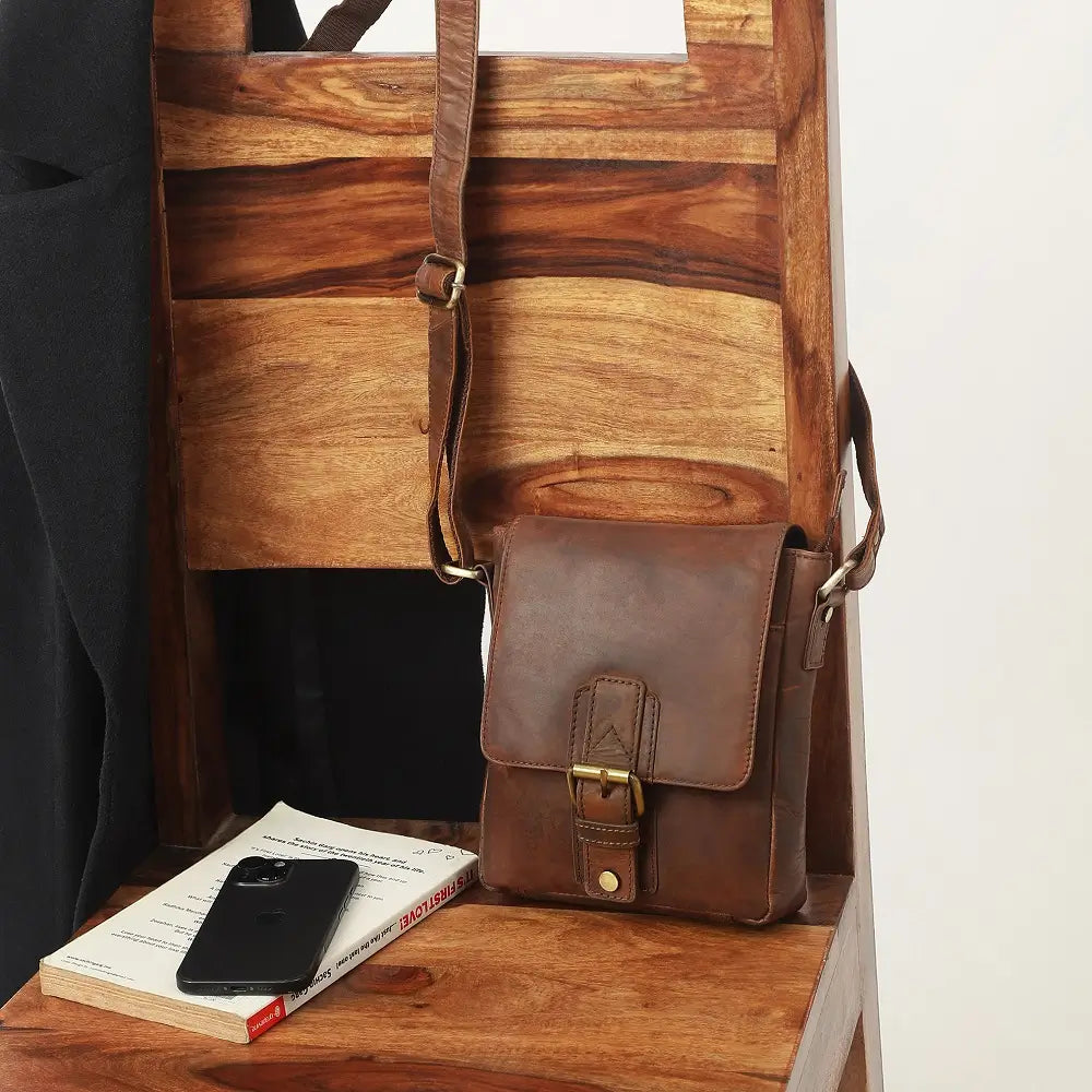 Brown leather bag on a wooden surface with a phone and book