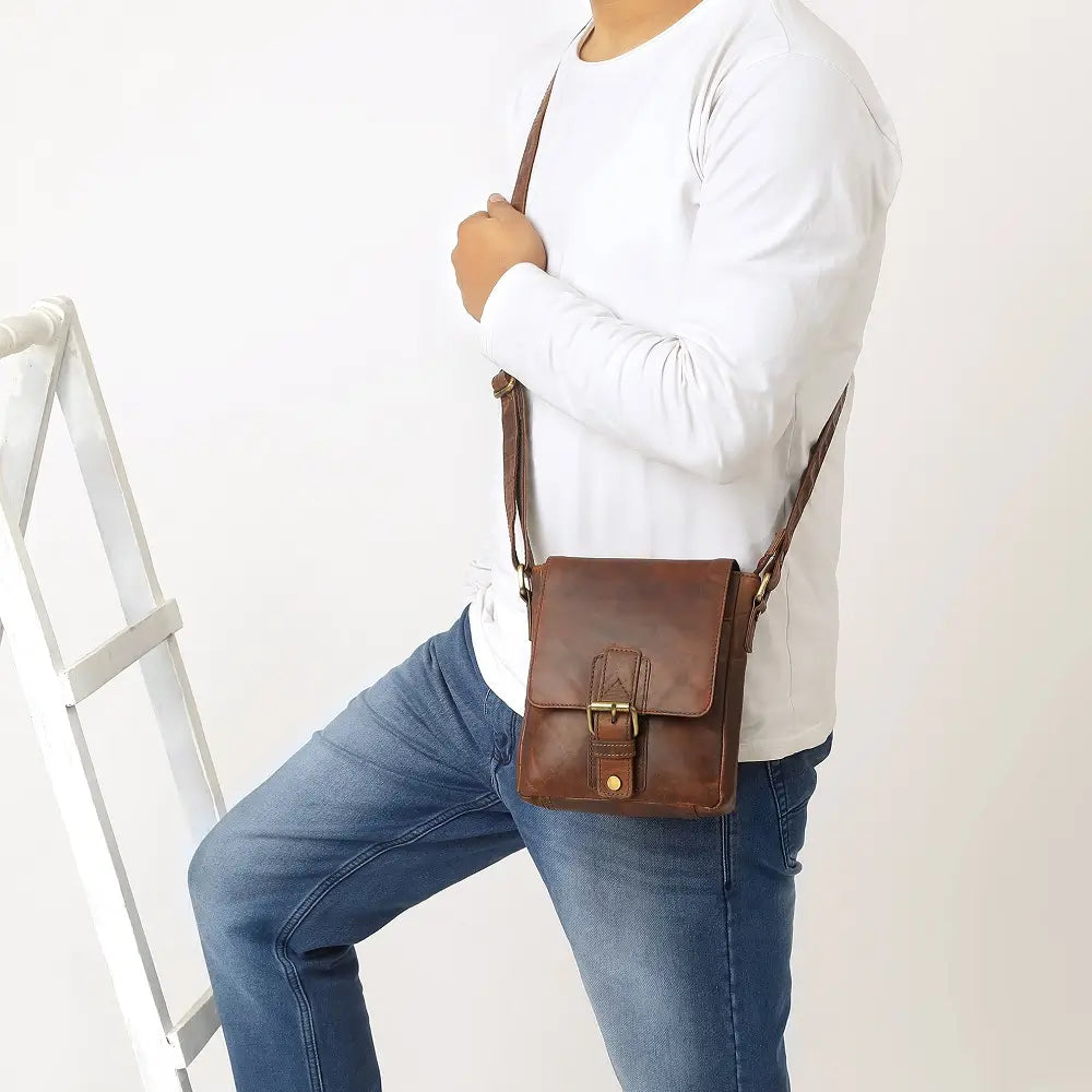 Brown leather crossbody bag with gold buckles on a white background