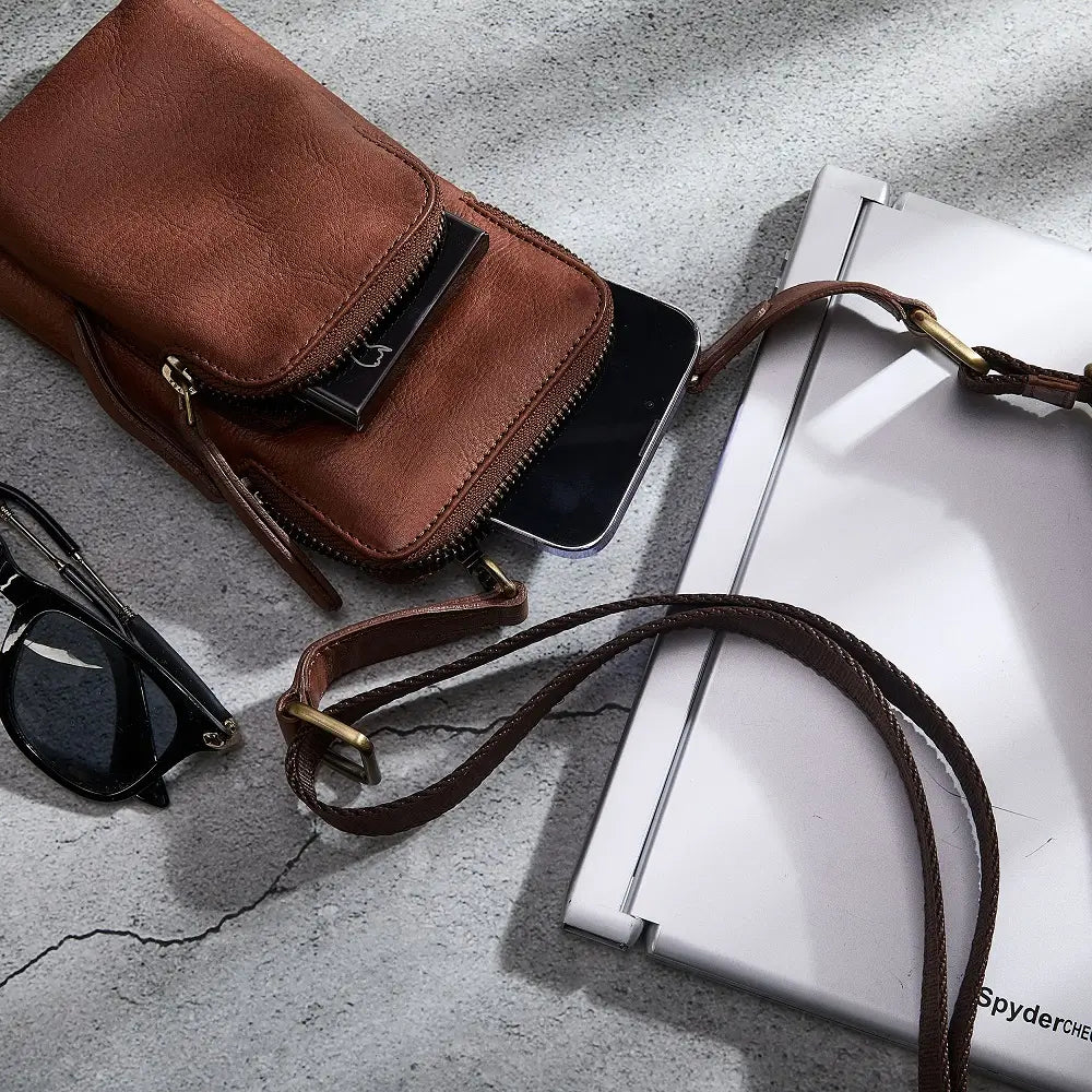 Brown leather phone bag with sunglasses on a textured surface
