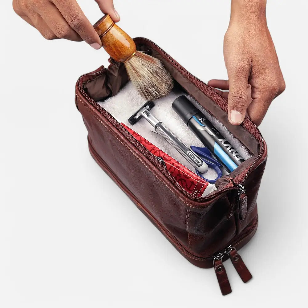 Brown leather toiletry bag with grooming products on a white background