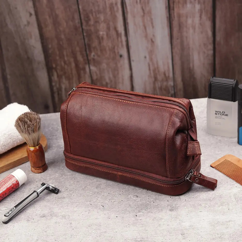 Brown leather toiletry bag on a wooden surface with grooming items.