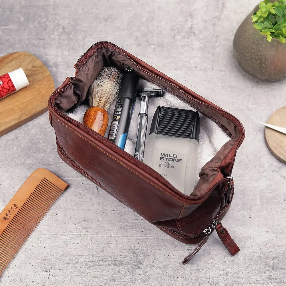 Open brown leather toiletry bag with grooming products on a light gray surface.