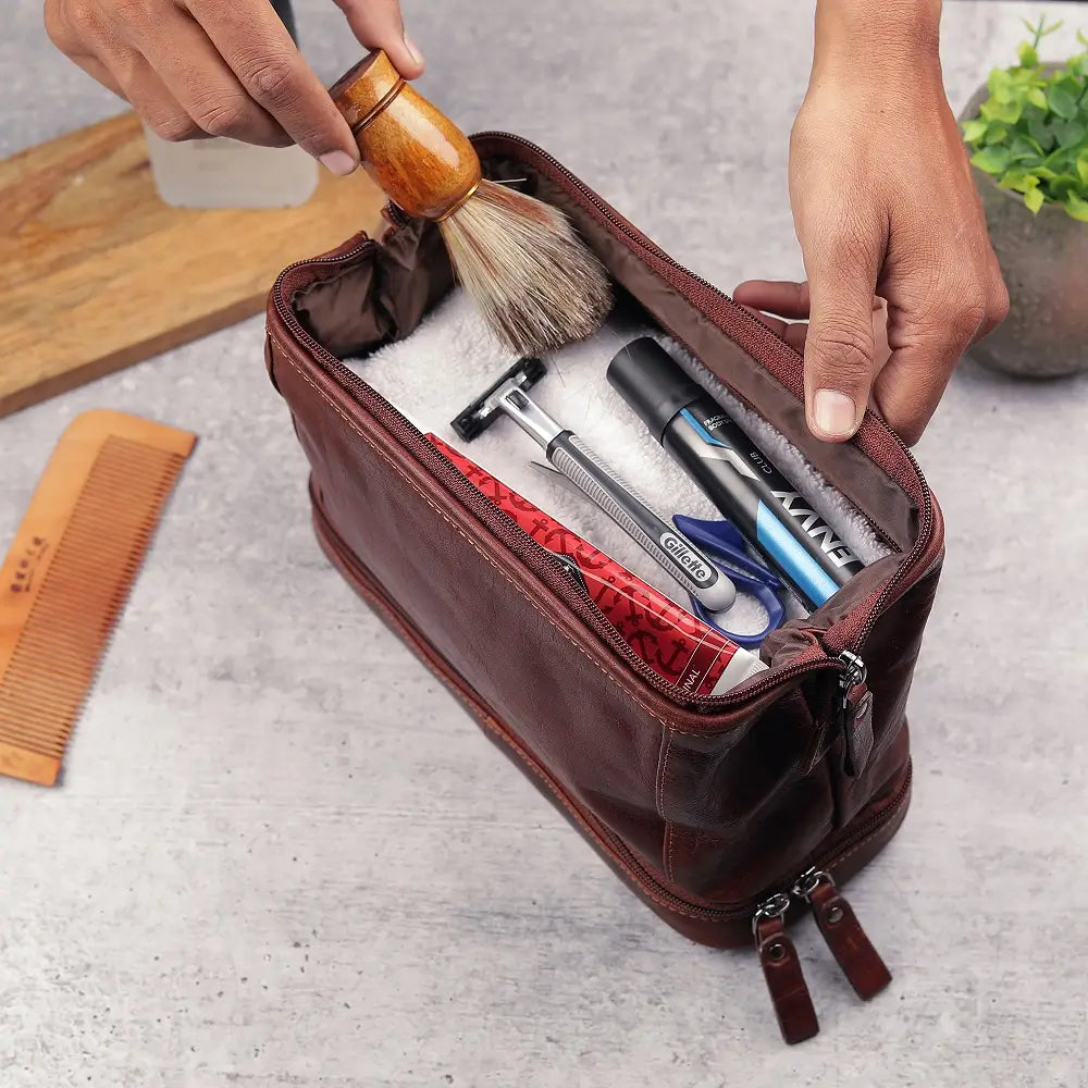 Brown leather toiletry bag with grooming tools on a light gray surface