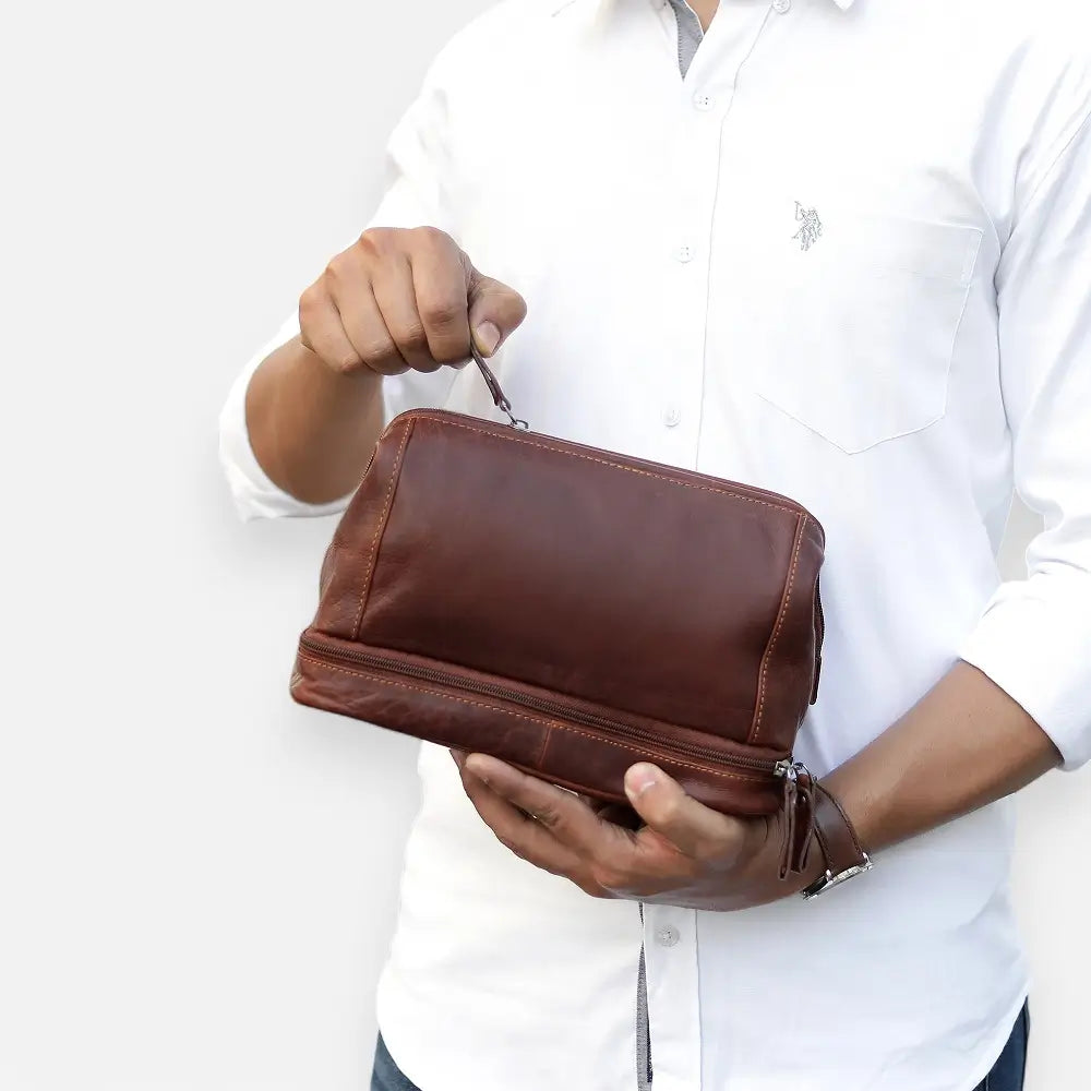 Person holding a brown leather toiletry bag against a white background
