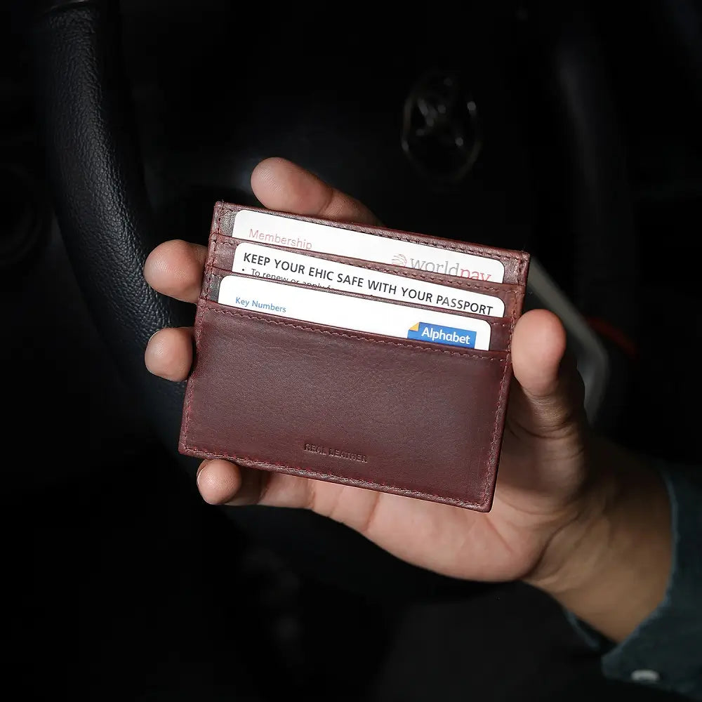 Hand holding a brown leather card holder with visible cards against a dark background