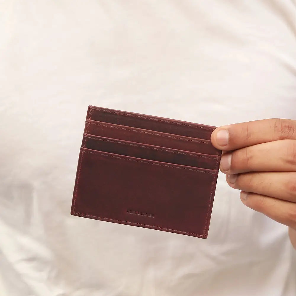 Brown leather cardholder held by a hand against a white background