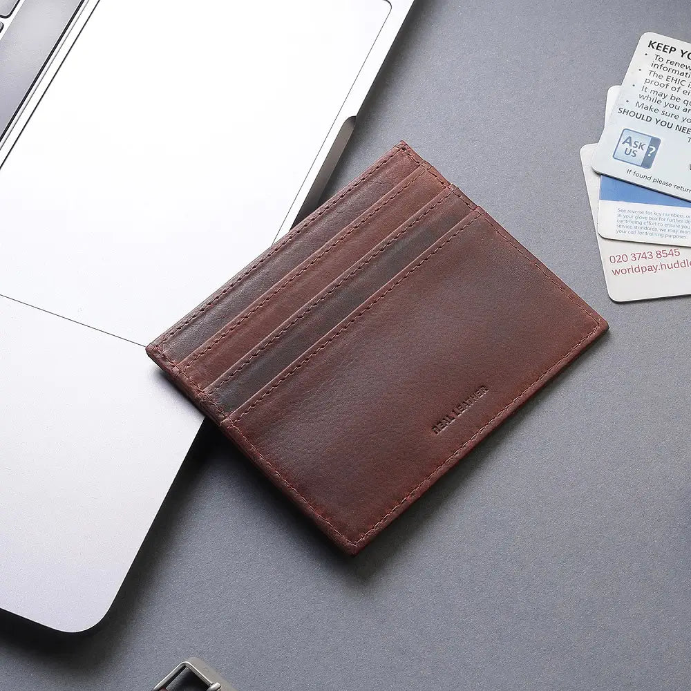 Brown leather cardholder on a gray surface with a laptop and cards in the background