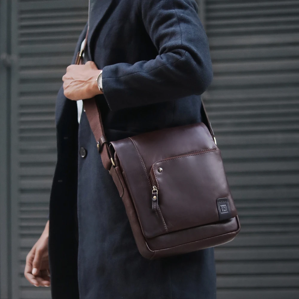 Person holding a brown leather bag against a gray background