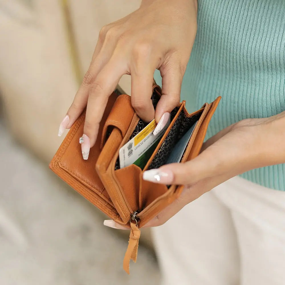 Person opening a cognac leather wallet with cards inside, wearing a light blue top.