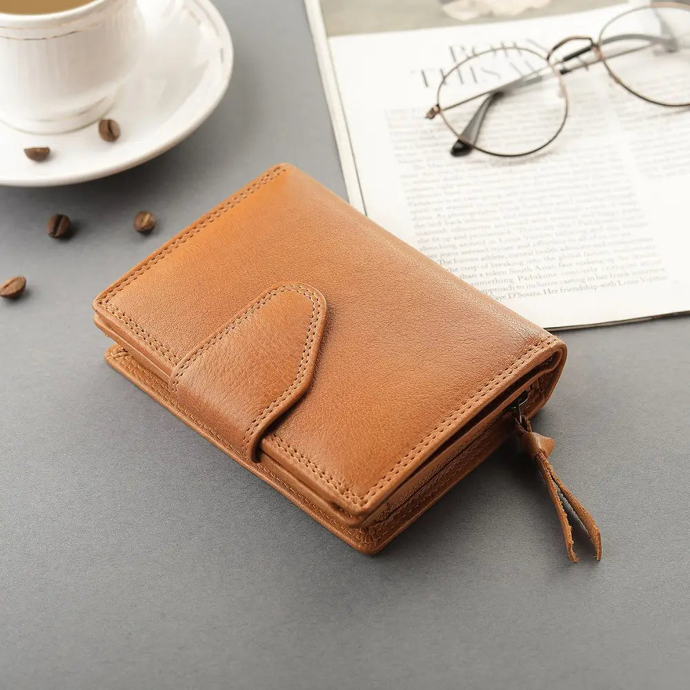 cognac leather wallet on a gray surface with a cup, saucer, and glasses in the background.