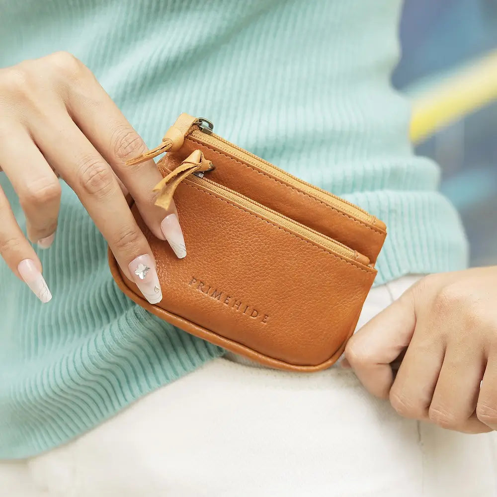 Cognac leather wallet with 'TRIMENHIDE' branding held by a person against a blurred background.