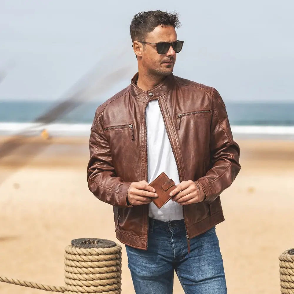 Man wearing a cognac leather jacket and sunglasses on a beach.