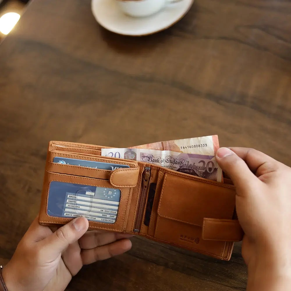 Lifestyle view of Cognac leather wallet with money and cards held by hands on a wooden table.