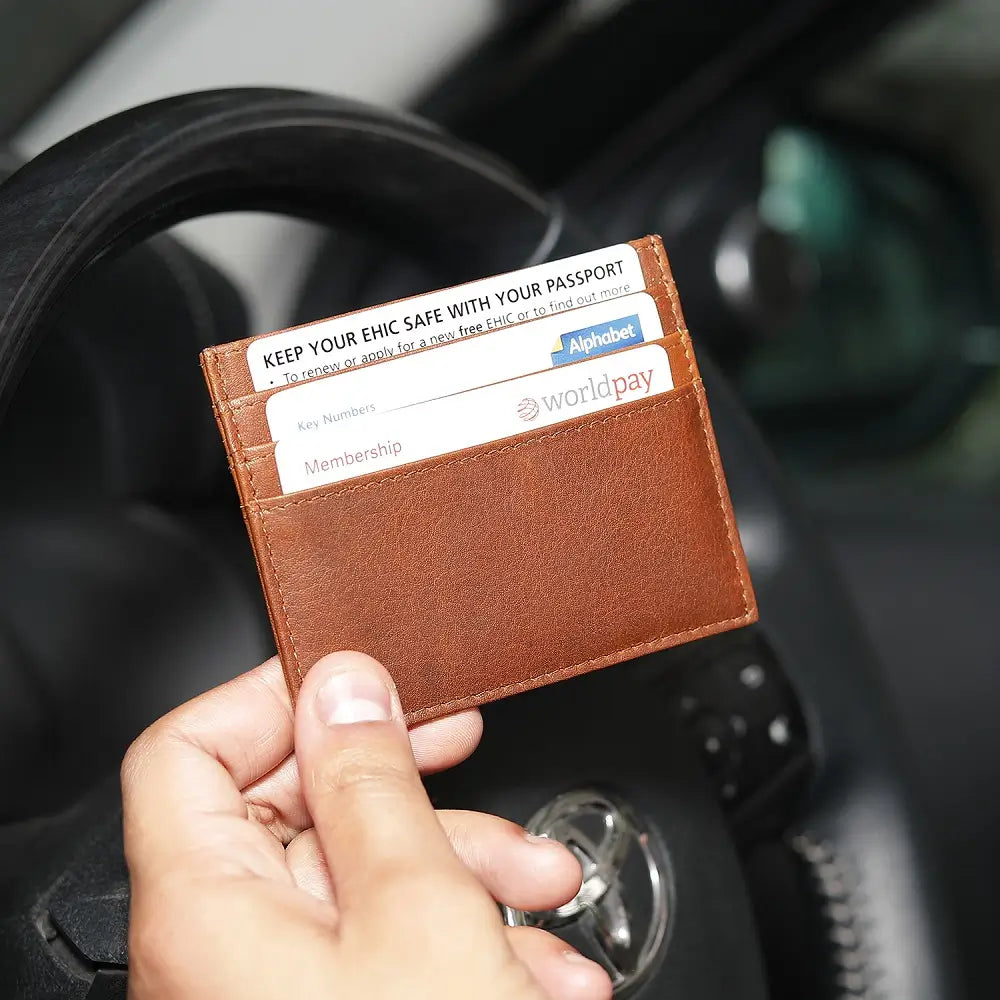 Cognac leather card holder with cards held by a hand inside a car.