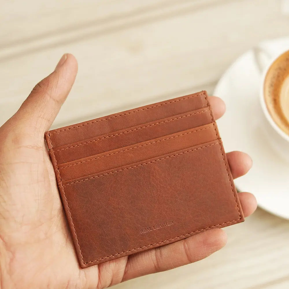 Cognac  leather cardholder held in a hand with a blurred coffee cup in the background