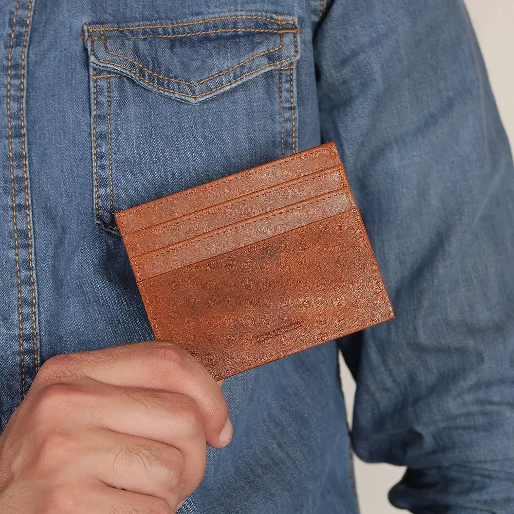 Cognac leather card holder held by a person wearing a blue denim jacket.